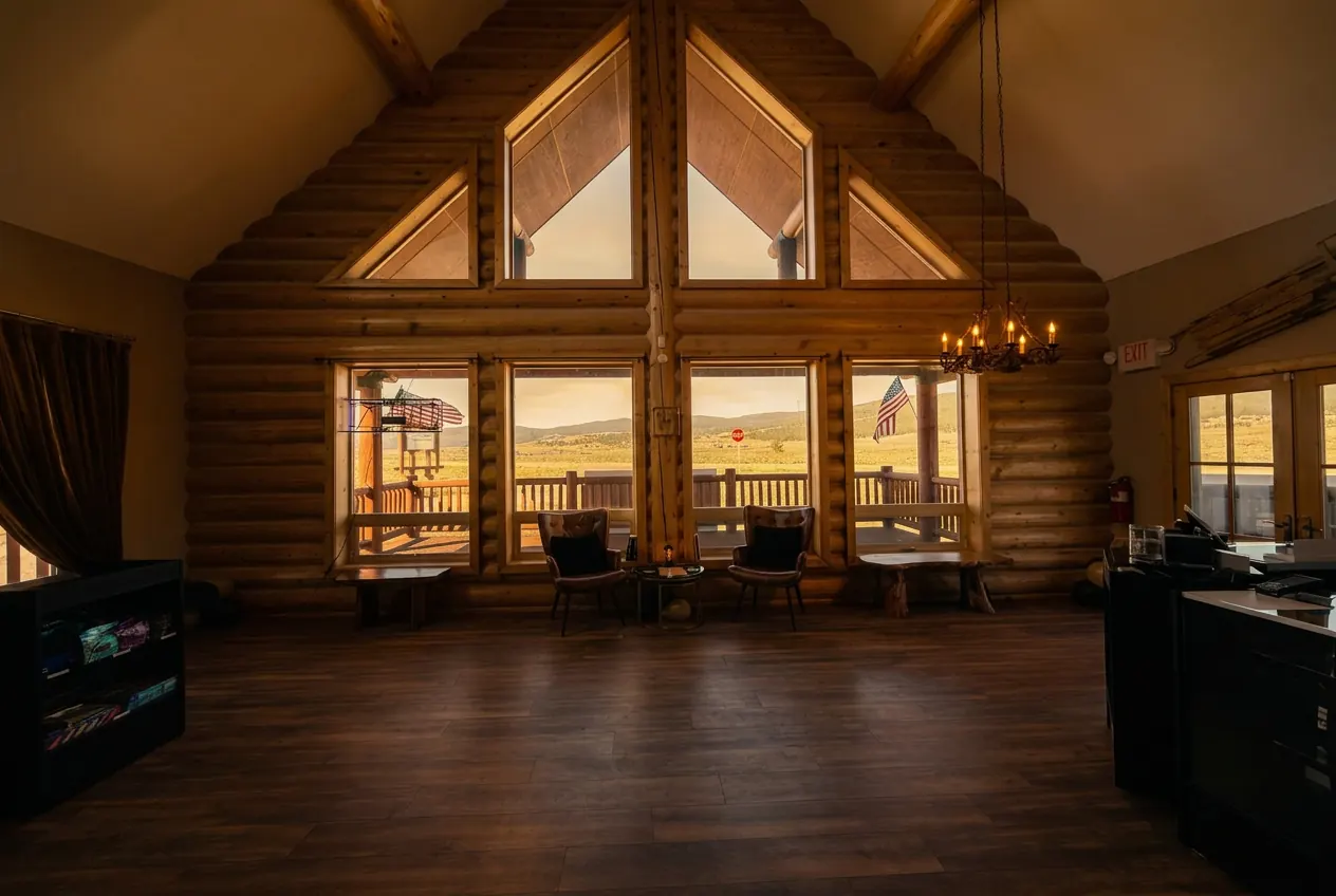 Inside Vesper in Angel Fire: vaulted log cabin ceiling, A-frame windows facing the mountains, leather chairs, and the counter on the right